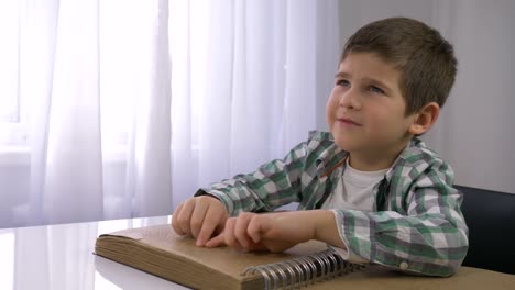 niño-ciego-leyendo-el-libro-Braille-con-la-fuente-de-símbolos-para-discapacitados-visuales-sentados-en-la-mesa