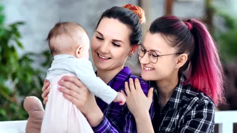 Mujeres-felices-padres-sosteniendo-pequeño-hijo-jugando-y-admirando-lindo-bebé-de-cerca