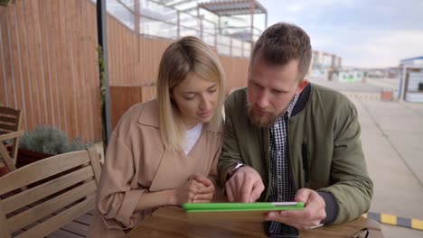 Spouses-are-discussing-and-examining-electronic-catalog-in-tablet,-sit-in-cafe