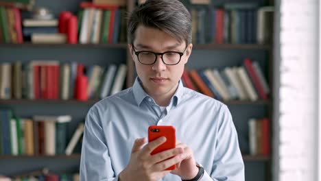 young-man-portrait-using-smartphone-laughing-standing-in-library-social-media-funny