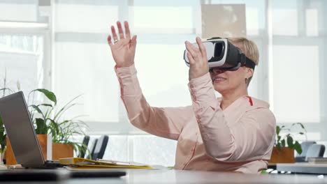 Mature-businesswoman-trying-3d-virtual-reality-glasses-at-her-workplace