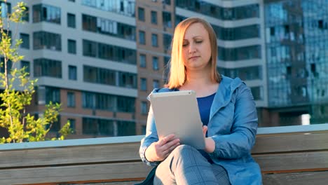 Frau-mit-Tablet-Computer-sitzt-auf-Bank-in-der-Stadt