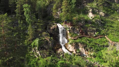 Drohne-fliegt-über-einen-grünen-Wald-mit-Wasserfall-im-Altai-Gebirge