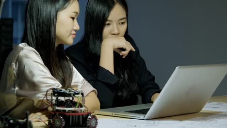 Asian-young-electronics-engineer-using-laptop-to-research-information-to-make-robot-together.-Technology-and-innovation-concept.