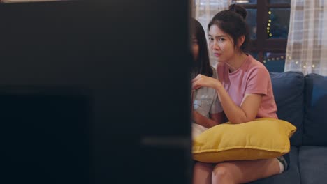 Lesbian-lgbt-women-couple-watching-movie-at-home,-Asian-female-lover-eating-popcorn-scary-and-shock-while-looking-horror-film-together-on-sofa-in-living-room-in-night-concept.-Slow-motion-shot.