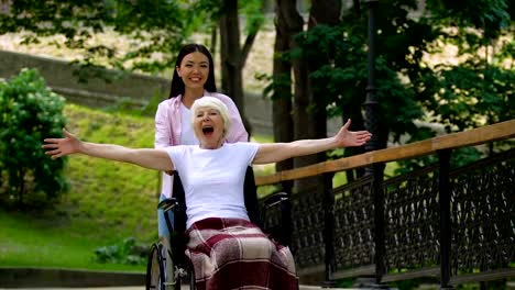 Smiling-volunteer-in-park-with-inspired-old-woman-in-wheelchair-raising-hands