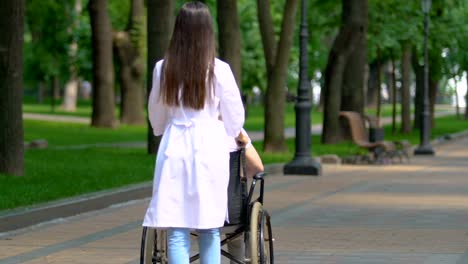 Nurse-carrying-disabled-patient-of-nursing-home-in-wheelchair-through-park