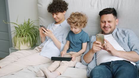 Mann-und-Frau-mit-Smartphones,-während-Kind-spielen-Spiel-auf-Tablet-im-Bett-zu-Hause