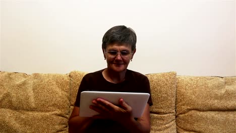 Attraktive-erwachsene-Frau-arbeiten-auf-ihrem-Tablet,-während-auf-einem-Sofa-zu-Hause-sitzen.