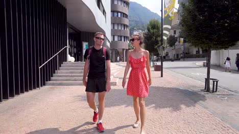 pair-of-tourists-are-walking-in-small-city,-chatting-and-looking-landmarks,-man-and-woman-are-strolling