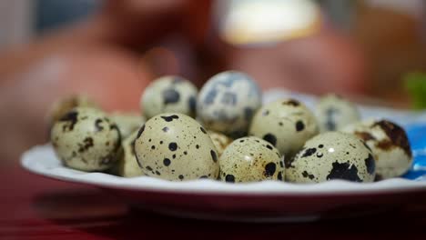 Female-hand-takes-small-quail-egg-from-the-plate-on-table-at-night-asian-market.-Closeup-of-fresh-quail-eggs