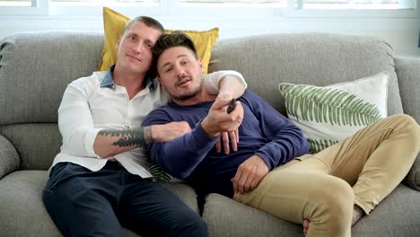 Pareja-gay-relajándose-en-el-sofá-viendo-la-televisión.-Abrazando-cómodamente.