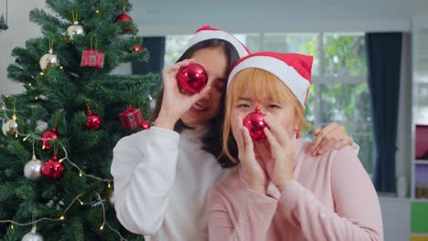 Asian-Lesbian-couple-celebrate-Christmas-festival.-LGBTQ-female-teen-wear-Christmas-hat-relax-happy-play-Christmas-ball-enjoy-xmas-winter-holidays-together-in-living-room-at-home.-Slow-motion-shot.