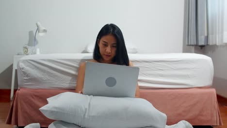 Junge-asiatische-Frau-mit-Laptop-Überprüfen-Social-Media-Gefühl-glücklich-lächeln,-während-auf-dem-Bett-liegen-duponieren,-nachdem-sie-morgens-im-Haus-aufwachen,-attraktive-thai-Mädchen-lächelnd-entspannen-im-Schlafzimmer-zu-Hause-Konzept.