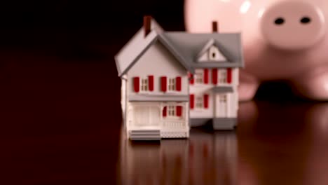 Pan-of-Piggy-Bank-and-Miniature-House-on-Dark-Wood-Surface