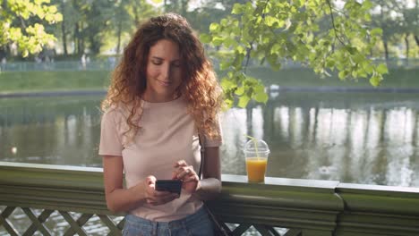 Mujer-feliz-usando-el-teléfono-en-el-parque-en-el-día-soleado