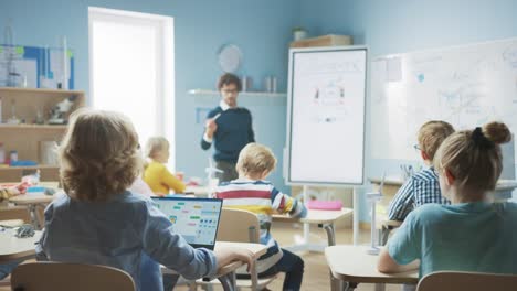 Grundschulphysiklehrer-verwendet-interaktives-digitales-Whiteboard,-um-einem-Klassenzimmer-voller-intelligenter-Verschiedener-Kinder-zu-zeigen,-wie-Generator-funktioniert.-Science-Class,-Kid-Raises-Hand-mit-Antwort