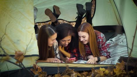 Happy-tourists-using-smartphone-lying-in-tent