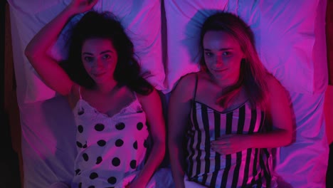 Attractive-girls-falling-on-bed-together-and-looking-at-camera,-night-seduction