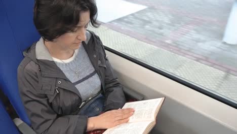 Caucasian-woman-middle-aged-riding-a-train-reading-a-book