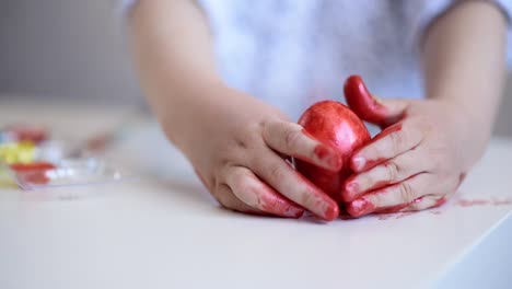 Un-niño-pequeño-pinta-un-huevo-de-pascua-en-la-mesa-sobre-un-fondo-blanco.