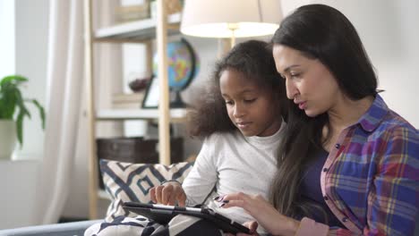 Mother-and-brunette-kid-is-sitting-on-sofa-and-using-electring-digital-technology