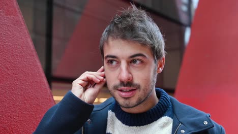 Handsome-young-man,-putting-on-wireless-earphones-while-standing-in-urban-city-background.