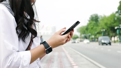 Close-up-hands-young-woman-typing-a-message-on-a-smartphone-while-standing-beside-the-street-in-urban.