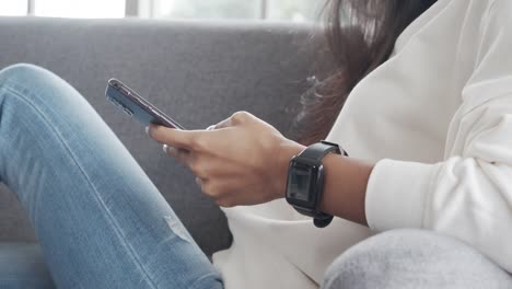 Close-up-hands-asian-female-using-smartphone-checking-social-media-and-shopping-online-store-while-laying-on-a-sofa-in-the-living-room-at-home-during-pandemic-coronavirus.