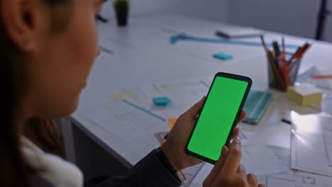 Business-woman-swiping-through-mobilephone-green-screen-at-her-office