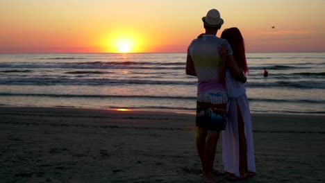 Pareja-abrazándose-y-besándose-en-la-orilla-de-una-playa-al-atardecer