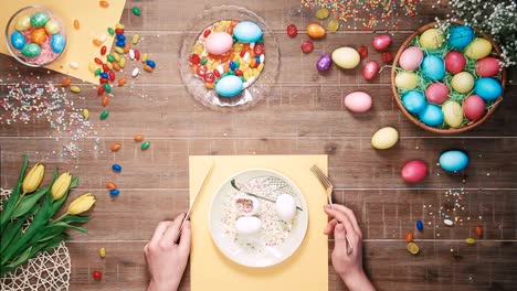 Man-holding-knife-and-fork-before-plate-with-easter-eggs-on-table-decorated-with-easter-eggs.-Top-view