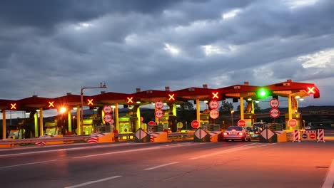 Carretera-coche-Paytoll-en-el-amanecer,-las-luces-de-noche-y-Autos-pasando-por-cabinas-de-peaje,-pagar-por-usar-la-carretera-y-autopista