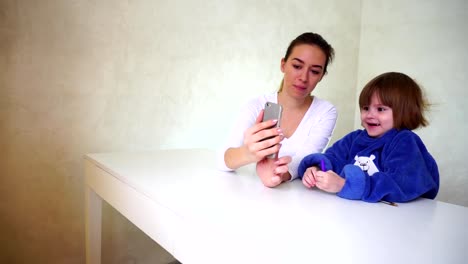 Young-mother-and-little-daughter-playing-with-phone-camera,-girls-sitting-and-using-funny-camera-effects