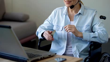 Disabled-female-consultant-with-headset-talking-with-client,-working-on-laptop