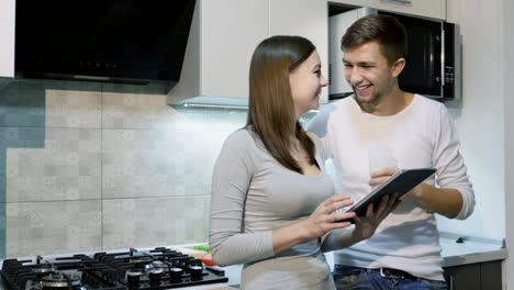 Pareja-feliz-en-su-casa-en-la-cocina-usando-tableta-juntos