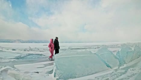 Young-couple-has-fun-during-winter-walk-against-background-of-ice-of-frozen-lake.-Lovers-walk-on-ice,-hold-each-other-by-hand,-kiss-and-hug.-Honeymoon.-Love-story.