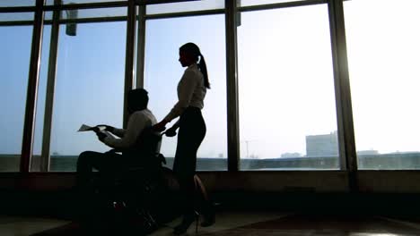 Businesswoman-Pushing-Businessman-on-Wheelchair-in-Office-Building