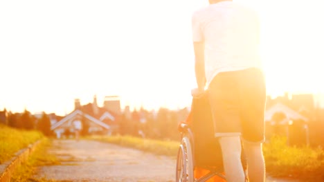 Guy-rollt-Mädchen-im-Rollstuhl-an-einem-Sommerabend-In-den-Sonnenuntergang