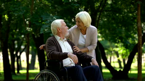 Caring-woman-supporting-her-husband-in-wheelchair,-kissing-each-other,-family