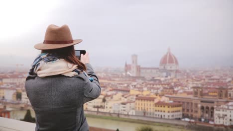 Happy-young-female-traveler-walks-up,-taking-smartphone-photo-of-amazing-cityscape-panorama-of-autumn-Florence,-Italy.