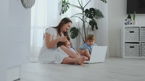 Moderne-Wohnung-Mutter-und-zwei-Söhne-auf-dem-Boden-im-Wohnzimmer-Blick-auf-den-Laptop-Bildschirm