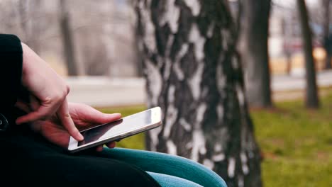 Junge-Frau-mit-Smartphone-auf-einer-Bank-im-Stadtpark