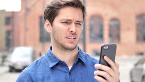 Outdoor-Portrait-of-Young-Man-Upset-by-Loss-while-Using-Smartphone