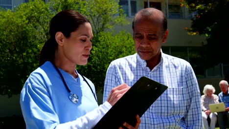 Front-view-of-active-Asian-senior-man-and-female-doctor-discussing-over-medical-report-in-the-garden