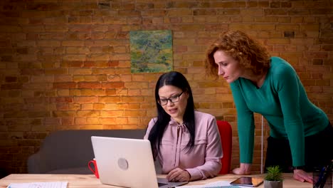 Nahaufnahme-von-zwei-Geschäftsfrauen,-die-über-Daten-auf-dem-Laptop-im-Büro-diskutieren.-Geschäftsmann-vorbeiziehen-und-grüßen