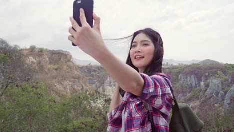 Blogger-Asian-backpacker-woman-record-vlog-video-on-top-of-mountain,-young-female-happy-using-mobile-phone-make-vlog-video-enjoy-holidays-on-hiking-adventure.-Lifestyle-women-travel-and-relax-concept.