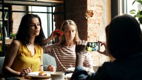 Mujeres-despreocupadas-posando-para-la-cámara-del-teléfono-inteligente-en-el-café-sosteniendo-la-flor-divirtiéndose