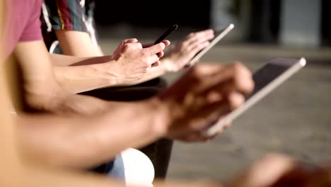 People-sitting-on-wooden-bench-and-using-digital-devices