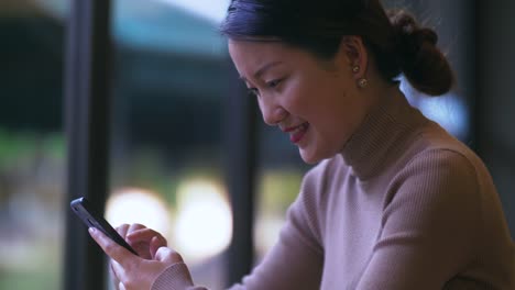 Fröhliche-junge-chinesische-Geschäftsfrau-mit-Handy-drinnen